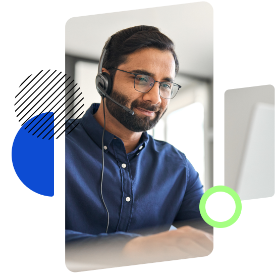 A man wearing glasses and a headset, smiling while working at a computer, likely engaged in a virtual meeting or support session.